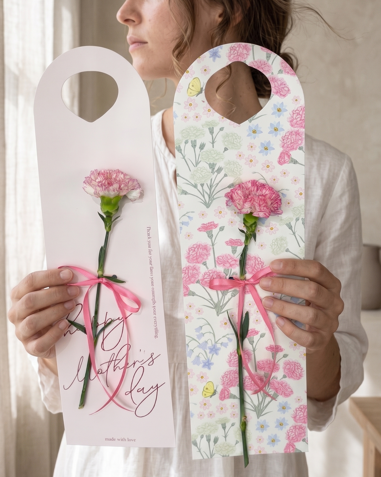 Woman holding two floral Mother's Day cards with pink ribbons.